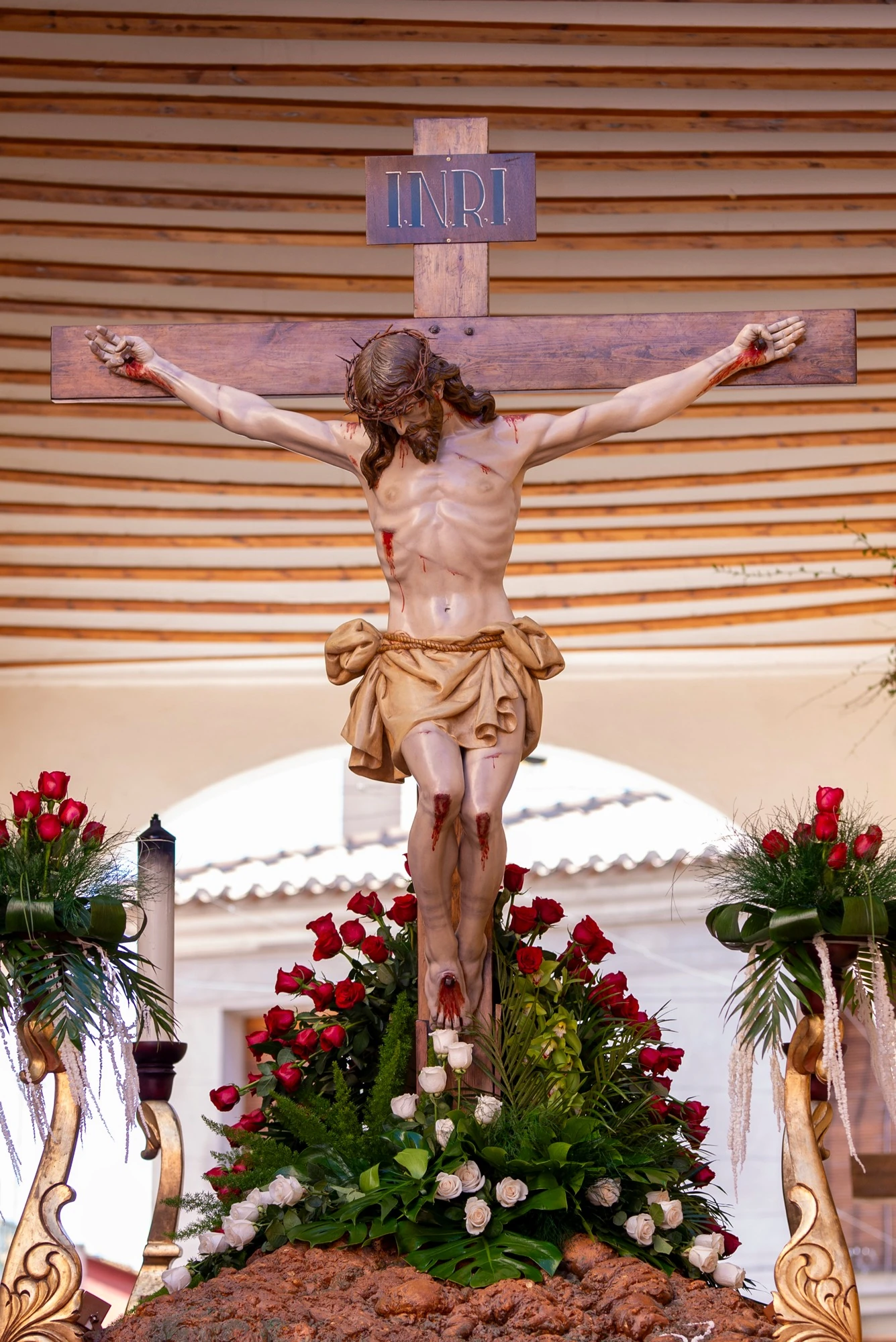 Vista frontal de Cristo Crucificado con su cruz y el adorno floral del trono