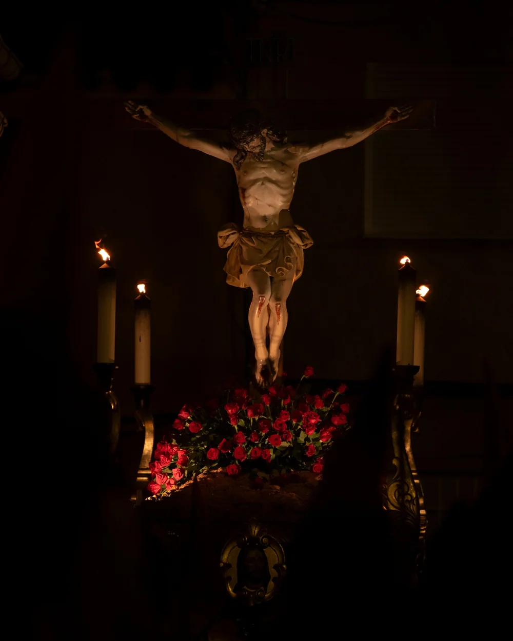El Cristo Crucificado entre cirios encendidos y flores rojas